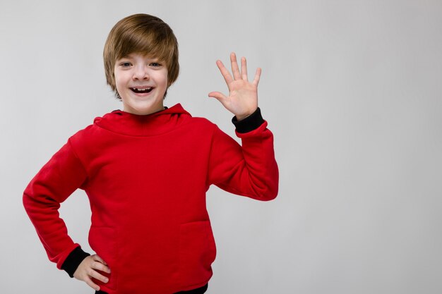 Leuke zekere Kaukasische kleine jongen in rode sweater die open palm op grijs toont