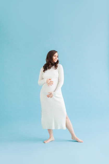 Leuke zwangere vrouw in witte jurk op blauwe achtergrond.