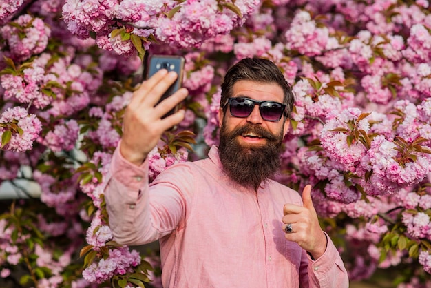 Leven in het moment Lente roze sakura bloesem Man selfie maken met mobiele telefoon brute volwassen hipster smartphone gebruiken in kersenbloesem bebaarde man geniet van sakura bloesem gevoel gelukkig