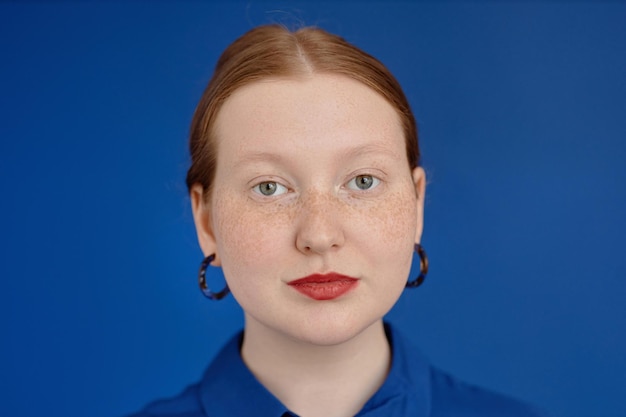 Levendige close-up roodharige jonge vrouw die camera op blauw bekijkt