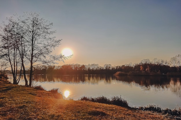 Levendige herfst zonsondergang. Herfst landschap van zonsondergang over rivier met glanzend gras op de wal. Schilderachtige natuur op heldere avond met kleurrijke lucht