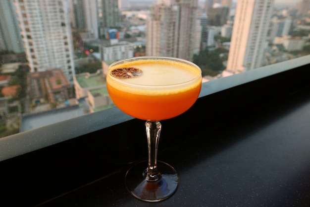 Levendige oranje cocktail op de bar op het dak met luchtfoto stedelijke weergave