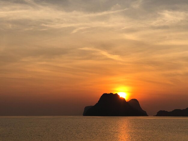 Levendige oranje zonsondergang boven de rotsachtige oceaankust met silhouetstrand en bewolkte hemel op een zomeravond