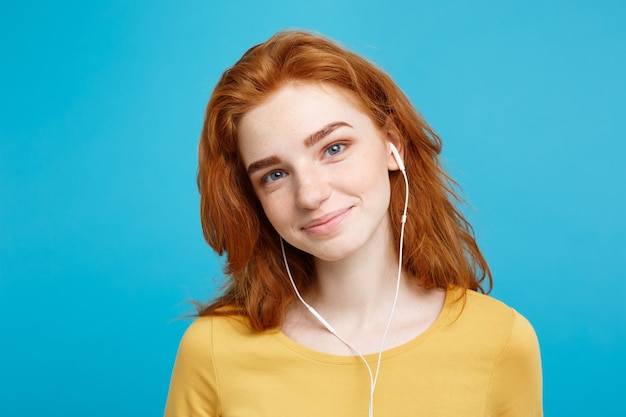 Levensstijl concept portret van vrolijk gelukkig gember rood haar meisje geniet van het luisteren naar muziek met koptelefoon blij lachend geïsoleerd op blauwe pastel muur kopie ruimte