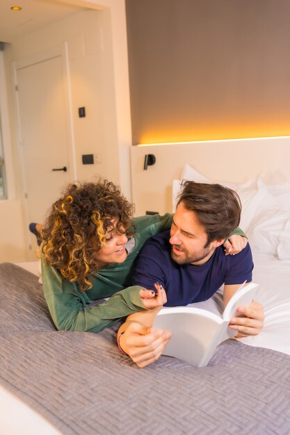 Levensstijl, een jong Kaukasisch stel, in pyjama's in bed lezen van een mooi boek omarmd