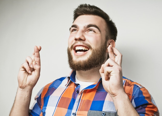 Levensstijl en mensenconcept: wachten op een speciaal moment. Portret van een jonge, bebaarde man in shirt die vingers houdt terwijl hij tegen een witte achtergrond staat. Hipsterstijl en positieve emoties.