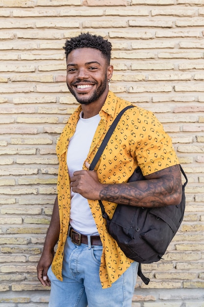 Levensstijl portret van een aantrekkelijke jonge man met baard met een rugzak met een bakstenen muur