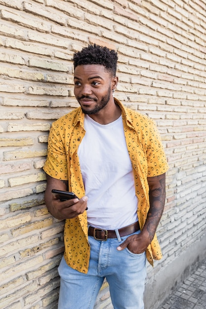 Levensstijl portret van een knappe amerikaanse man met behulp van een smartphone in de straat met bakstenen muur