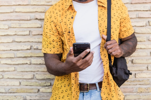 Levensstijl portret van een knappe Amerikaanse man met behulp van een smartphone in de straat met bakstenen muur