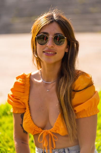 Levensstijl van een jonge blanke brunette die van de zomer geniet in een park in de stad. Meisje met zonnebril en een oranje t-shirt