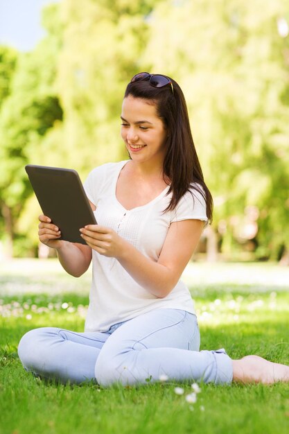 levensstijl, zomer, vakantie, technologie en mensenconcept - glimlachend jong meisje met de computer van tabletpc zittend op gras in park