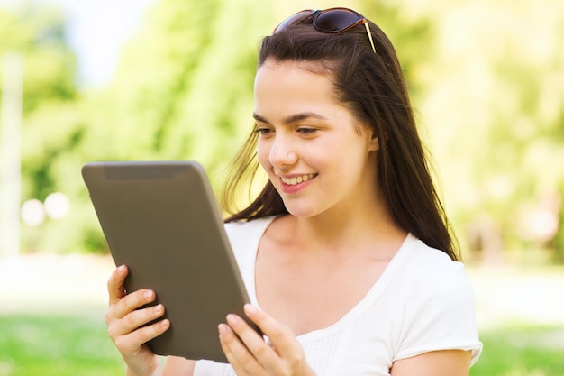 levensstijl, zomer, vakantie, technologie en mensenconcept - glimlachend jong meisje met de computer van tabletpc zittend op gras in park