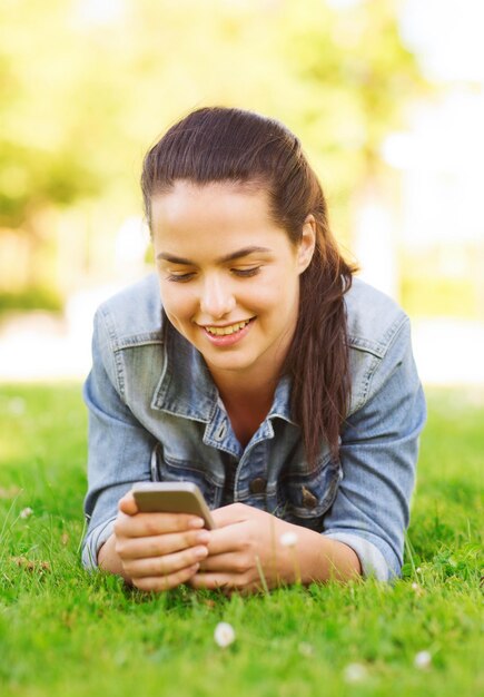 levensstijl, zomervakantie, technologie, vrije tijd en mensenconcept - glimlachend jong meisje met smartphone die op gras in park liggen