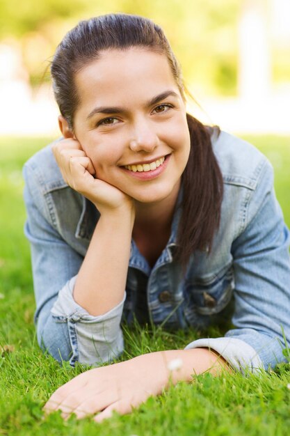levensstijl, zomervakantie, vrije tijd en mensenconcept - glimlachend jong meisje dat op gras in park ligt