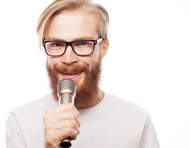 Levensstijlconcept: een jonge man met een baard die een wit overhemd draagt dat een microfoon vasthoudt en zingt. Geïsoleerd op wit.