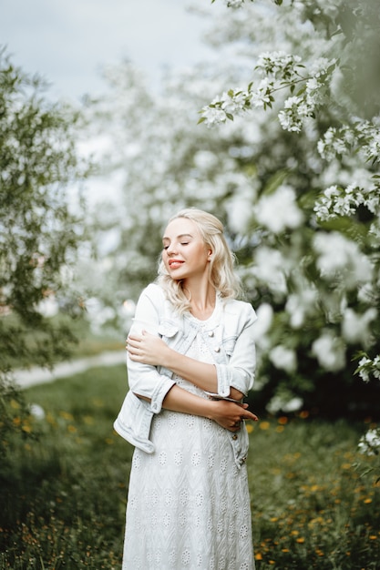 Levensstijlconcept: een jonge vrouw die gelukkig tegen een achtergrond van bloeiende bomen glimlacht