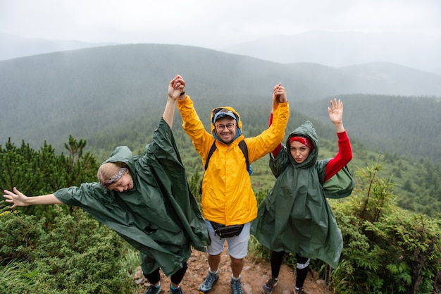 Levensstijlportret van opgewekte lachende groep reizigers in regenjassen hoog in bergen.