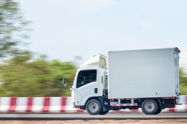 Lever een kleine witte vrachtwagen die op een groen natuurlijk pad rijdt tegen de achtergrond van een wolkenhemel