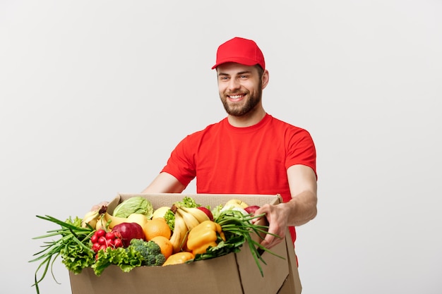 Levering concept: knappe blanke bezorger koerier man in rood uniform met boodschappen doos