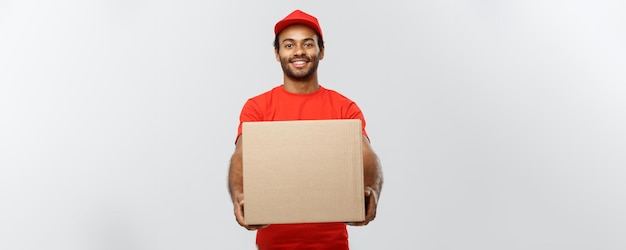 Levering concept portret van gelukkige Afro-Amerikaanse bezorger in rode doek met een doos pakket geïsoleerd op grijze studio achtergrond kopie ruimte