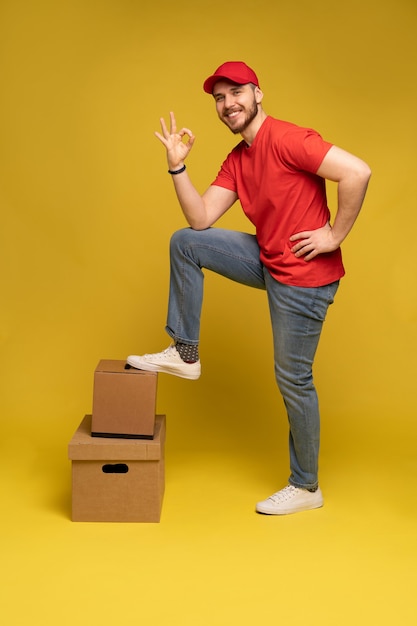 Levering man met doos in studio geïsoleerd op gele muur