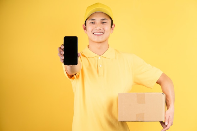 Levering mannelijke portret lading doos houden en vooruit telefoon op gele muur te houden