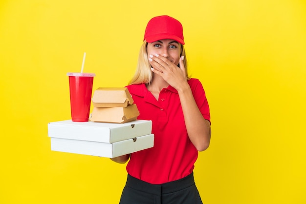 Levering Uruguayaanse vrouw met fastfood geïsoleerd op gele achtergrond, blij en glimlachend die mond bedekt met hand