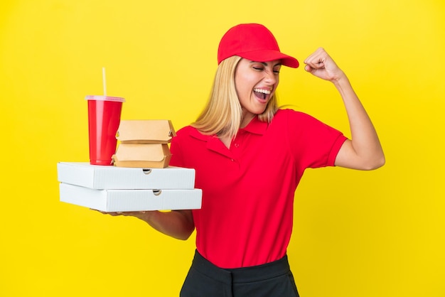 Foto levering uruguayaanse vrouw met fastfood geïsoleerd op gele achtergrond die een overwinning viert