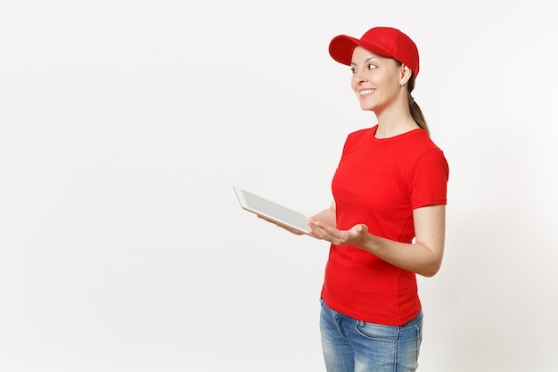 Levering vrouw in rode uniform geïsoleerd op een witte achtergrond. Vrouw in pet, t-shirt, spijkerbroek die werkt als koerier of dealer, met tablet pc-computer met leeg leeg scherm. Ruimte voor advertentie kopiëren
