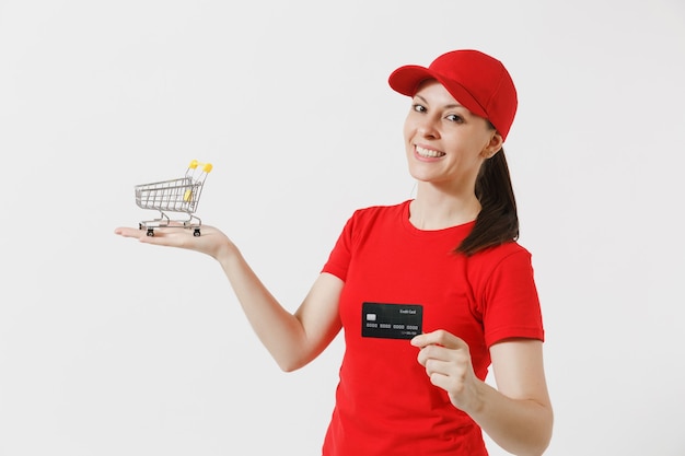 Levering vrouw in rode uniform geïsoleerd op een witte achtergrond. vrouwelijke koerier of dealer in pet, t-shirt met supermarkt boodschappenwagentje om te winkelen, creditcard. kopieer ruimte voor advertentie.