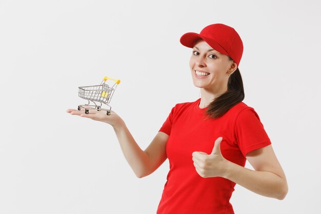 Levering vrouw in rode uniform geïsoleerd op een witte achtergrond. Vrouwelijke koerier of dealer in pet, t-shirt, spijkerbroek met supermarkt boodschappenwagentje om te winkelen op palm. Kopieer ruimte voor advertentie.