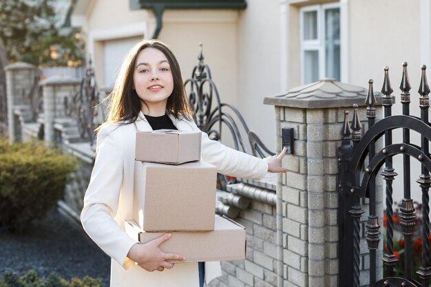 Leveringsconcept het meisje staat in de buurt van het huis en houdt dozen in handen