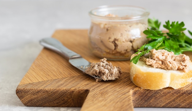 Leverpastei in een glazen pot met vers brood en peterselie op een houten snijplank.