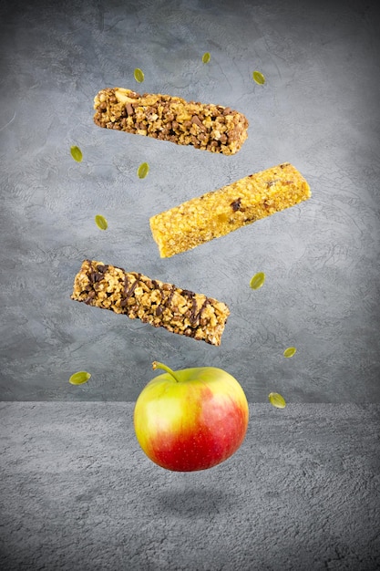 Levitating food three muesli bars ripe yellow red apple and a\
few green seeds over gray surface