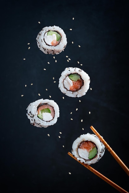Foto rotoli di sushi giapponesi levitanti a base di riso alga nori, salmone crudo, crema di formaggio e cetriolo