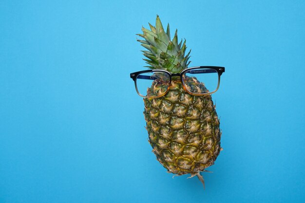 Levitating pineapple with glasses on a blue background with copy space