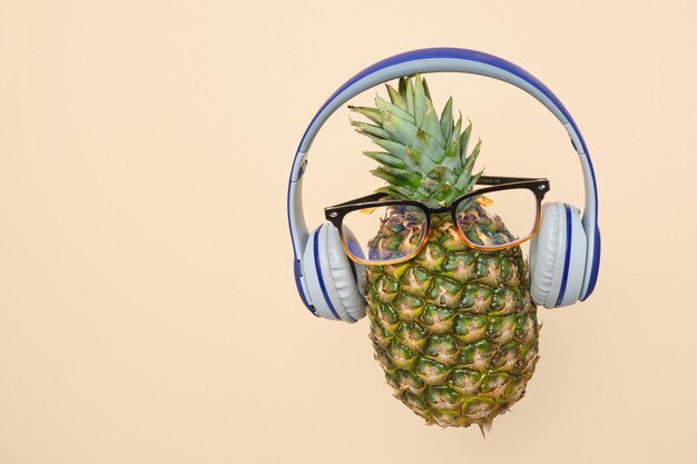 Photo levitating pineapple with glasses and headphones on a light yellow background with copy space