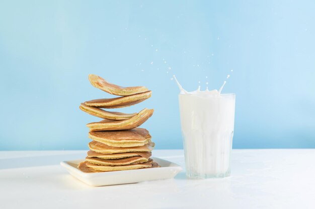 Levitating stack of pancakes with honey and glass of milk. Splash of milk from the glass on a blue background.  Levitation, gravity. Homemade breakfast.