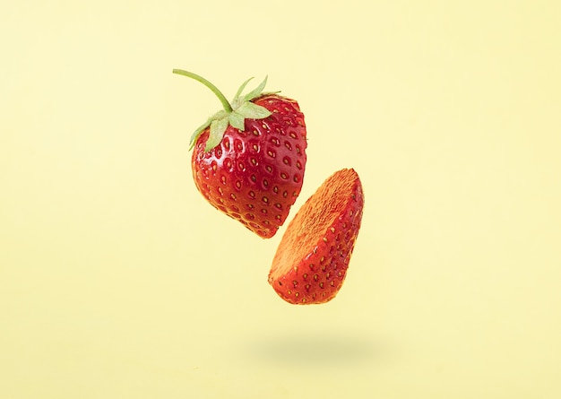 Levitation of sliced strawberries against a trendy minimal pastel yellow and contemporary background