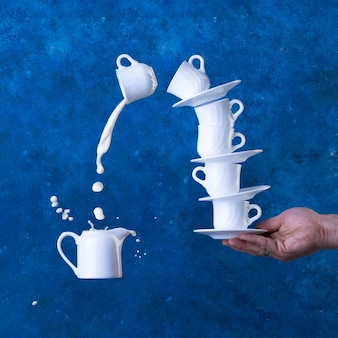 Levitazione con tazze e latte con spruzzi su sfondo blu. concetto.