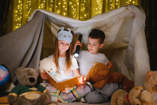 Lezen en familiespelletjes in kindertent jongen en meisje met boek en zaklamp voor het naar bed gaan