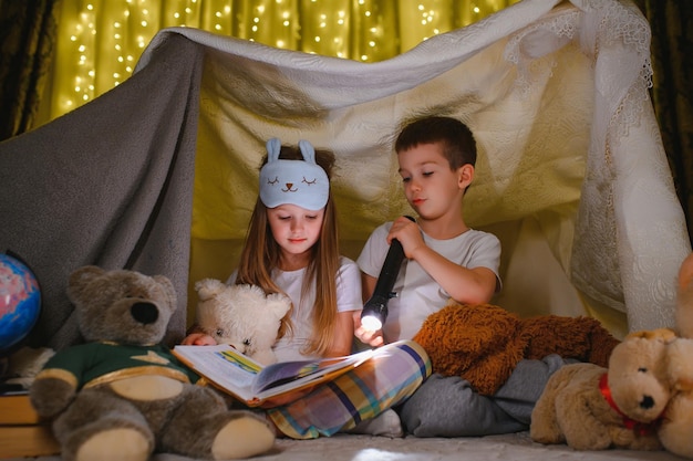 Lezen en familiespelletjes in kindertent jongen en meisje met boek en zaklamp voor het naar bed gaan