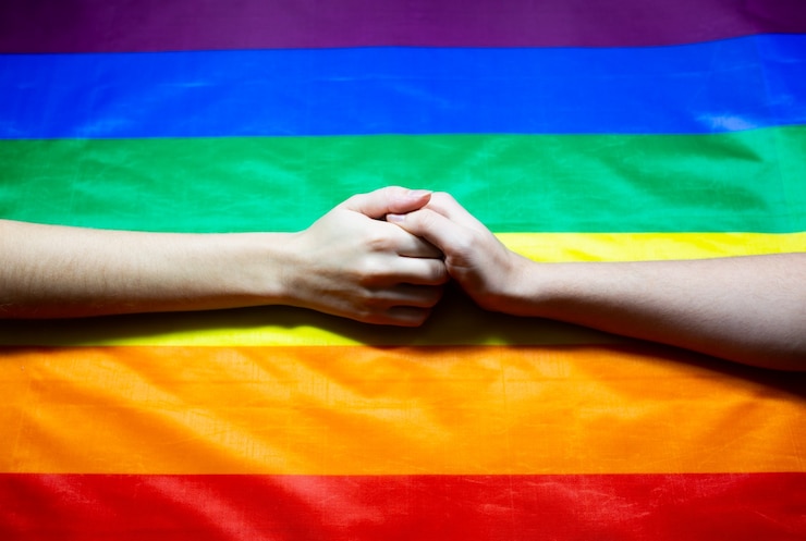 Photo lgbtコミュニティのカラフルな旗。虹の背景に2人の女性の手。レズビアンとゲイの問題。同性愛指向のカップルのための結婚の合法化。