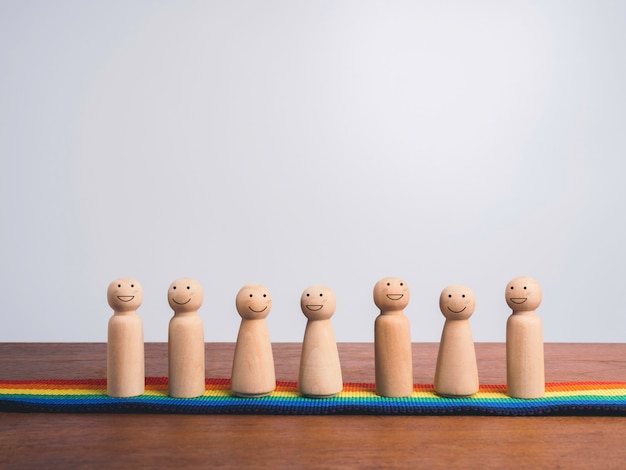 Foto concetto di comunità lgbt. gruppo di figure in legno con facce sorridenti felici in piedi insieme sulla bandiera arcobaleno, parata dell'orgoglio su tavola di legno e sfondo bianco con spazio per le copie.