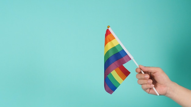 LGBT concept.Hand is holding a rainbow flag on mint green or tiffany blue background.