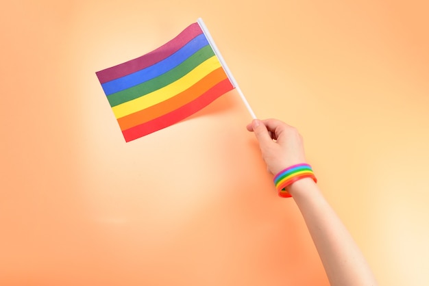 Флаг ЛГБТ в руке женщины на оранжевом фоне. Скопируйте пространство.