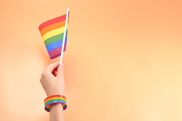 Флаг ЛГБТ в руке женщины на оранжевом фоне. Скопируйте пространство.