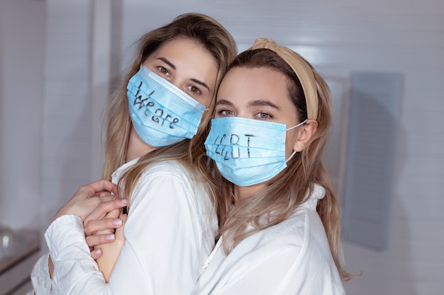 顔にサインが付いている医療保護マスクのLGBTレズビアンカップルは女性の瞬間の幸福の概念を愛する