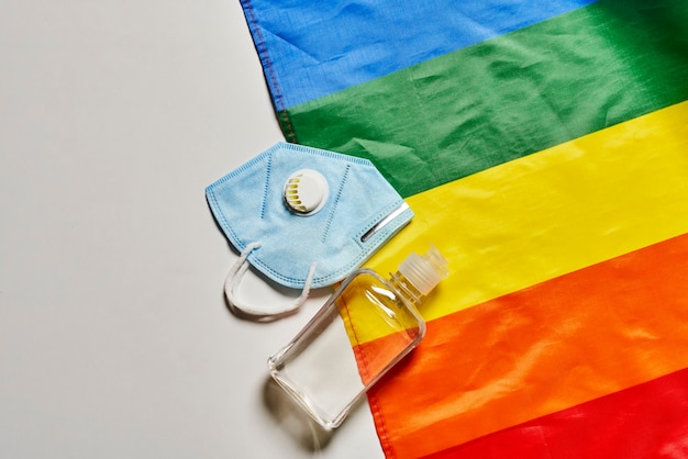 Foto lgbt-regenboogvlag en covid-artikelen voor persoonlijke hygiëne gezichtsmasker n gasmasker en fles desinfectiemiddel