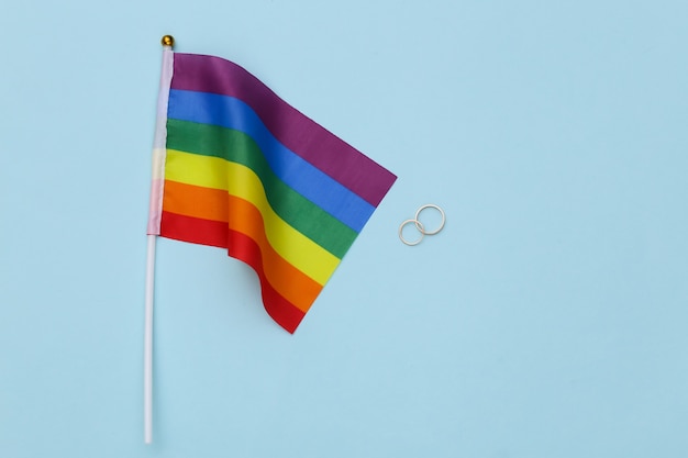 LGBT wedding. LGBT rainbow flag and golden rings on blue background. Tolerance, freedom